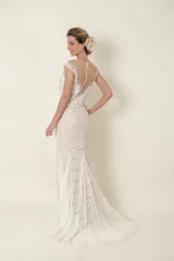 Vestido largo de novia color marfil, de encaje y tul, con apliques bordados y piedras. Tiene escote profundo y falda con cola.