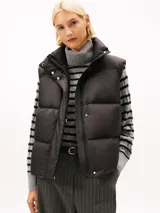 Chaleco acolchado de corte regular, confeccionado en poliéster reciclado. Presenta cuello alto con cierre de botones a presión, cierre frontal de cremallera oculto y diseño sin mangas. Incluye detalles distintivos y logo de la marca.