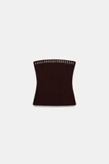 Top tipo bandeau de tejido elástico en color marrón oscuro, con escote recto y hombros descubiertos. Presenta una fila de tachas metálicas decorativas a lo largo del borde superior.