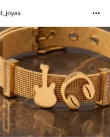 Pulsera de malla metálica con baño de oro, con dijes de guitarra y auriculares, y detalles de circonias en los extremos.