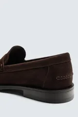 Mocasín de vestir para hombre, color marrón oscuro, fabricado en piel con acabado serraje (gamuza). Presenta un antifaz en el empeine con costuras visibles y suela a contraste con ligero tacón.