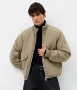 Campera bomber masculina de poliamida, con cuello, puños y ruedo de tejido elástico. Presenta cierre frontal con cremallera, dos bolsillos laterales con solapa y botón, y un pequeño bolsillo con cierre en una de las mangas.