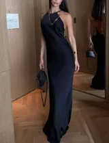 Vestido largo negro de silueta ajustada y escote halter. Presenta espalda descubierta con tiras finas y un aplique metálico con pedrería de strass.