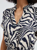 Vestido corto con estampado animal print tipo cebra en tonos blanco y negro. Presenta escote en V, mangas cortas y un lazo ajustable en la cintura para entallar la silueta.