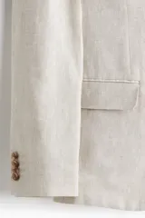 Blazer de lino liviano color beige, con solapas de muesca finas y ojal decorativo. Presenta cierre de dos botones, bolsillo superior, bolsillos delanteros con solapa y dos bolsillos interiores. Tiene botones decorativos en los puños y abertura doble en la parte trasera. Forrado y con corte ajustado.