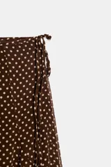 Falda midi de corte evasé con estampado de lunares, forro interior corto y detalle de lazo lateral con abalorios. Cuenta con cierre de cremallera oculta en la costura.
