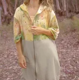 Campera larga con capucha y cierre frontal, con diseño abstracto en tonos amarillo, verde y rosa sobre fondo beige.