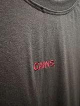 Remera unisex de corte oversize, color negro, confeccionada en algodón. Presenta un bordado frontal con la palabra 'GAINS.' en color rojo.