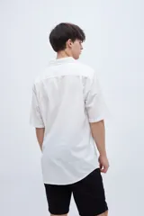 Camisa de manga corta en tela de algodón color blanco con rayas verticales en relieve y bolsillo en el pecho.