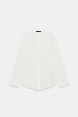 Camisa oversize blanca de cuello solapa y manga larga con puños anchos. Cuenta con cierre frontal de botones y un bolsillo aplicado en el frente.