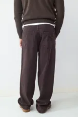 Pantalón estilo skater de corte holgado, color marrón oscuro, con cierre de botón y cremallera, bolsillos laterales y traseros.