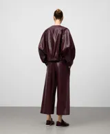 Pantalón culotte de mujer color bordó, confeccionado en viscosa con recubrimiento que simula piel. Presenta cierre frontal con botón, bolsillos laterales y bolsillos de vivo en la espalda. La pierna es ancha.
