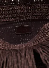 Bolso tipo sobre de fibra natural en color marrón, con diseño tejido y panel frontal de flecos largos.