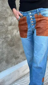 Pantalón de jean con apliques de cuero marrón en los bolsillos delanteros y en los tobillos.