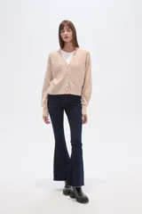 Cárdigan color beige de poliéster con cuello en V, corte al cuerpo y mangas abullonadas. Decorado con cuentas blancas.