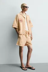 Shorts relaxed fit color beige con textura en relieve tipo jacquard, cintura elástica con cordón ajustable y detalle de bordado en contraste en el bajo.