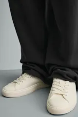 Zapatilla de cordones con diseño minimalista, parte superior lisa y suela con volumen. Presenta un detalle de pieza a contraste en la parte posterior.