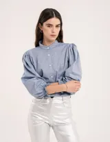 Blusa celeste de cuello mao y mangas abullonadas con puños elásticos. Tiene tajos laterales y botones en la delantera.