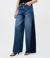 Pantalón de jean modelo wide leg con cintura media y cierre tradicional. Presenta un diseño bicolor con un recorte lateral en tono más oscuro que contrasta con el resto de la prenda, aportando una silueta alargada.