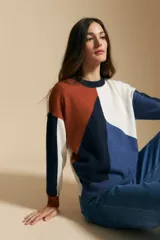Sweater de tejido de punto con diseño geométrico de bloques de color en tonos tierra, marrón, ocre y blanco. Presenta cuello redondo, mangas largas y un corte relajado.