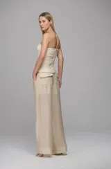 Pantalón de corte amplio y tiro alto, confeccionado en tejido ligero con paneles laterales transparentes y pliegues frontales. Presenta un diseño de pernera ancha con caída fluida y bolsillos laterales.