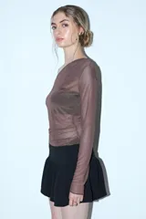 Remera de manga larga y escote asimétrico, confeccionada en tul negro transparente. Lleva un top negro opaco debajo y un cinturón de cadena plateada a la altura de la cadera.