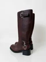 Bota de caña alta estilo biker, confeccionada en cuero negro. Presenta tres hebillas metálicas decorativas, cierre lateral y taco de madera.