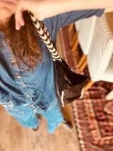 Bolso tipo tote de cuero negro con bolsillo externo y llavero interno. Tiene manijas cortas con diseño chevron y costuras blancas a contraste.