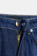 Jeans de denim azul oscuro, tiro alto, corte recto y pernera ancha, con raya planchada marcada en el frente y la espalda. Presenta cinco bolsillos y cierre frontal con botón dorado.