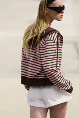 Sudadera de mezcla de algodón con capucha, cierre frontal de cremallera y bolsillos de plastrón delanteros. Presenta un diseño de rayas horizontales en tonos rosados, marrones y verdes, con acabados en rib elástico marrón en puños, cintura e interior de la capucha.