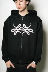 Hoodie con cierre frontal, color negro, de corte regular fit. Presenta un estampado frontal grande en blanco con un diseño abstracto y estilizado, similar a un monograma o símbolo.