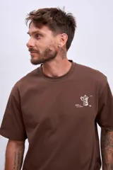 Remera blanca de manga corta con un pequeño estampado verde en el pecho que simula una caja abierta con un objeto dentro.