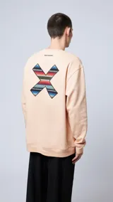 Sudadera color durazno de corte holgado con cuello redondo, puños y bajo acanalados. Estampado en la espalda con una cruz formada por motivos étnicos y logo de la marca en la parte superior.