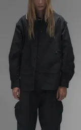 Chaqueta tipo overshirt de microfibra, color negro, con calce oversize y ruedo curvo. Presenta cierre frontal con broches a presión, bolsillos frontales de gran tamaño y cierres laterales a lo largo de las mangas para ajustar su amplitud.