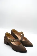 Zapato tipo Mary Jane de gamuza color marrón, con taco cuadrado medio y tira ajustable en el empeine con hebilla metálica dorada y detalles de ojalillos.