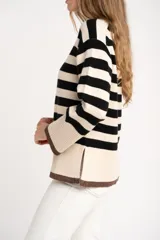 Sweater de punto a rayas horizontales negras y crudas, con cuello redondo y mangas largas. Tiene ribete marrón en puños y ruedo.