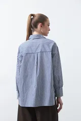 Camisa a rayas verticales blancas y marrones, de manga larga con puños abotonados, cuello camisero y botones frontales. Incluye un bolsillo en el pecho con bordado sutil.