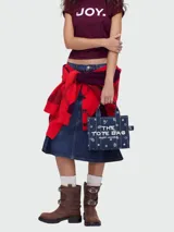 Cartera tipo tote bag de lona azul marino con estampado de motivos blancos y letras blancas bordadas en el frente. Cuenta con doble asa superior y cierre superior con cremallera.