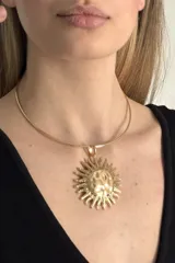 Gargantilla rígida de metal dorado con dije central grande en forma de sol con acabado texturizado.