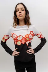 Remera de manga larga de algodón elastizado con diseño tricolor: blanca en la parte superior, negra en la parte inferior y una franja central estampada con flores y patrones geométricos en tonos rojos, blancos y verdes.