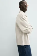 Polo de manga larga color crema, confeccionado en tejido de algodón, con cuello solapa y cierre frontal de botonadura. Presenta un calce relajado y acabados en rib en puños y ruedo.