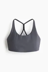 Top deportivo gris oscuro con soporte medio, confeccionado en tejido funcional con tecnología SculptMove™ y DryMove™. Cuenta con escote redondo, tirantes finos que se cruzan en la espalda y bajo elástico. Incluye copas con relleno extraíble.
