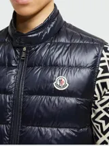 Chaleco de plumas Moncler modelo Gui, color azul marino, con diseño acolchado, cierre frontal con cremallera y cuello alto. Presenta el logo de la marca en el pecho.