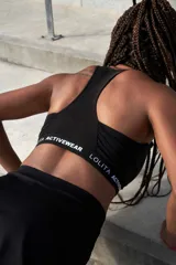 Top deportivo negro tipo halter con espalda deportiva y banda inferior con logo de la marca Lolita Activewear.