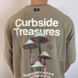 Remera negra de corte oversize con estampado gráfico en la espalda que presenta hongos en tonos violeta y verde, junto con la frase 'Curbside Treasures' y texto descriptivo.