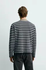 Camiseta de manga larga con ajuste relajado, confeccionada en tejido ligero de algodón. Presenta un diseño de rayas horizontales en color negro y blanco con cuello redondo.
