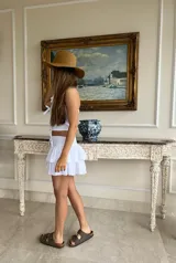 Top blanco confeccionado en algodón con cuello halter y detalle de tres lazos decorativos en el frente. Posee una textura ligera y un diseño romántico ideal para el verano.