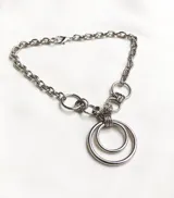 Collar plateado de cadena gruesa con eslabones grandes y dije de dos aros concéntricos.