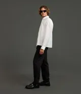 Pantalón de sastrería de corte recto, color negro con finas rayas verticales blancas. Presenta pliegues frontales, cintura ancha con trabillas para cinturón y cierre tradicional.