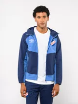 Campera deportiva Umbro del Club Nacional de Football, modelo Summit. Presenta un diseño con bloques de color en azul, rojo y blanco, con capucha, cierre frontal y bolsillos laterales con cierre. Incluye el logo de la marca y el escudo del club en el pecho.